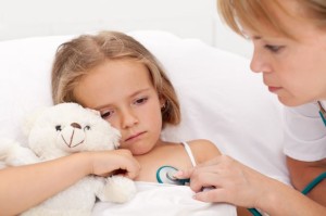 Sad little girl laying sick in bed checked by a doctor